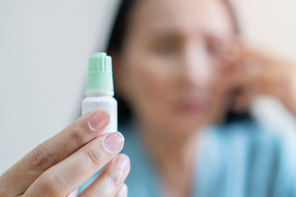 Closeup focus on eye drops, with person blurred in the back.