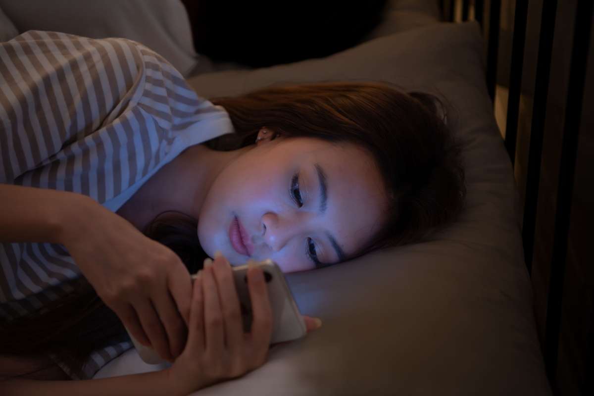 Young adult woman laying in bed looking at her phone up close.
